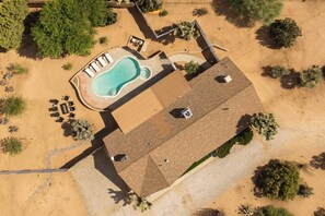 An aerial view of a property with a swimming pool, lounge chairs, and a patio area.
