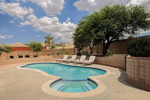 A swimming pool with a curved design, surrounded by a brick wall and a wooden fence. There are lounge chairs and a palm tree in the background.