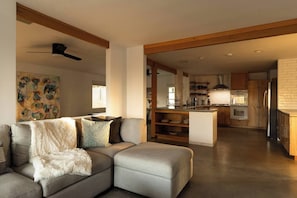 A modern living room with a grey sectional sofa, a white furry throw blanket, and a ceiling fan. - Black Rock Retreat - Desert Escape with Pool, Spa & Hammocks (Yucca Valley)