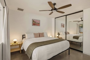 A bedroom with a bed, bedside lamps, a ceiling fan, a large mirror, and a window. - Black Rock Retreat - Desert Escape with Pool, Spa & Hammocks (Yucca Valley)