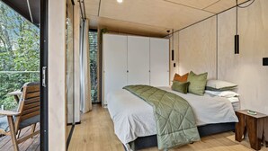 A modern bedroom with a bed, bedside table, and a view of greenery outside. - Okere Bush Retreat - Sauna, Spa, Sleeps 8 (Okere Falls)