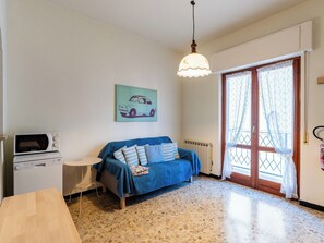 A room with a blue sofa, a small table, a microwave, and a painting of a car on the wall. - Nautilus by Interhome (Alassio)