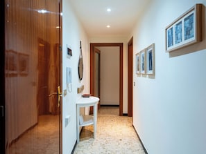 A hallway with a white door, a small table with a telephone, and framed pictures on the wall. - Nautilus by Interhome (Alassio)