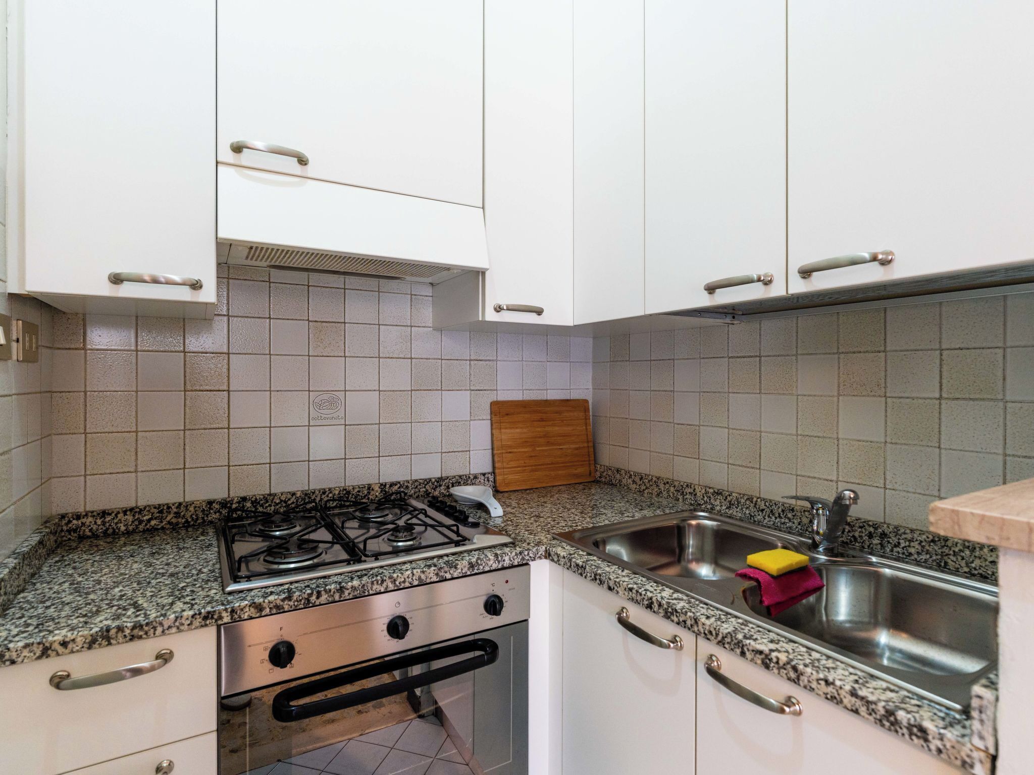 A kitchen with white cabinets, a gas stove, a sink, and a wooden cutting board.