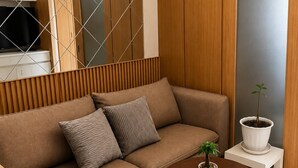 En moderne stue med en brun sofa, to puder, en lille potteplante og et rundt sofabord i træ.