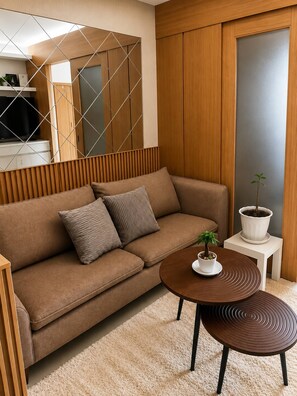 Ein modernes Wohnzimmer mit einem braunen Sofa, zwei Kissen, einer kleinen Topfpflanze und einem runden Holztisch.