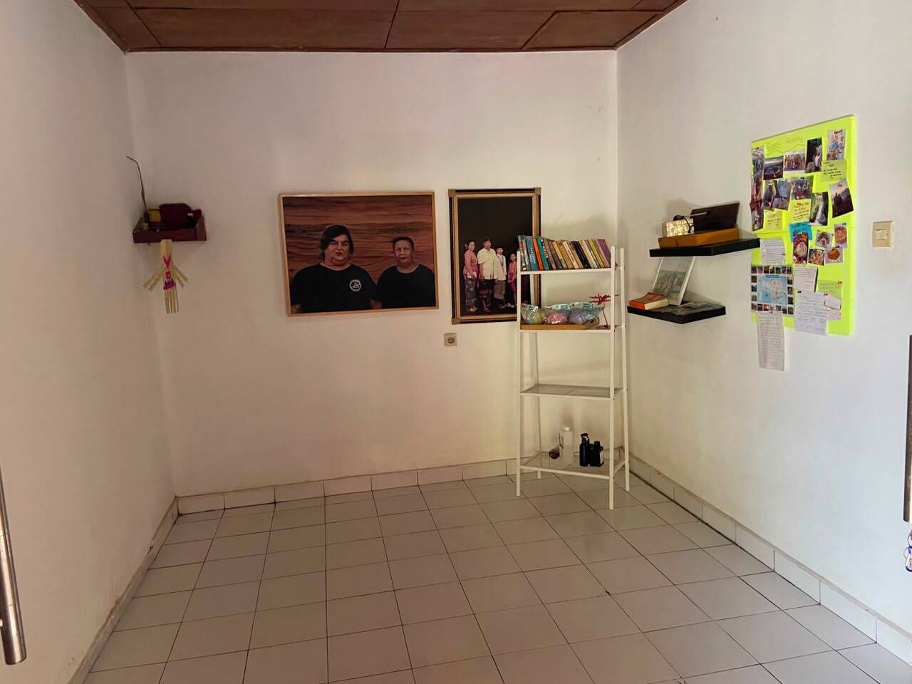 Een kamer met een betegelde vloer, een witte muur met een lijst, een witte plank met boeken, en een prikbord met aantekeningen.