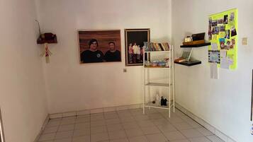 Een kamer met een betegelde vloer, een witte muur met een lijst, een witte plank met boeken, en een prikbord met aantekeningen.
