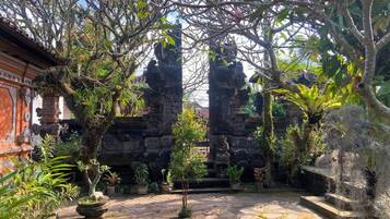 Un patio con senderos de piedra, plantas en macetas y una estructura de templo tradicional balinés.