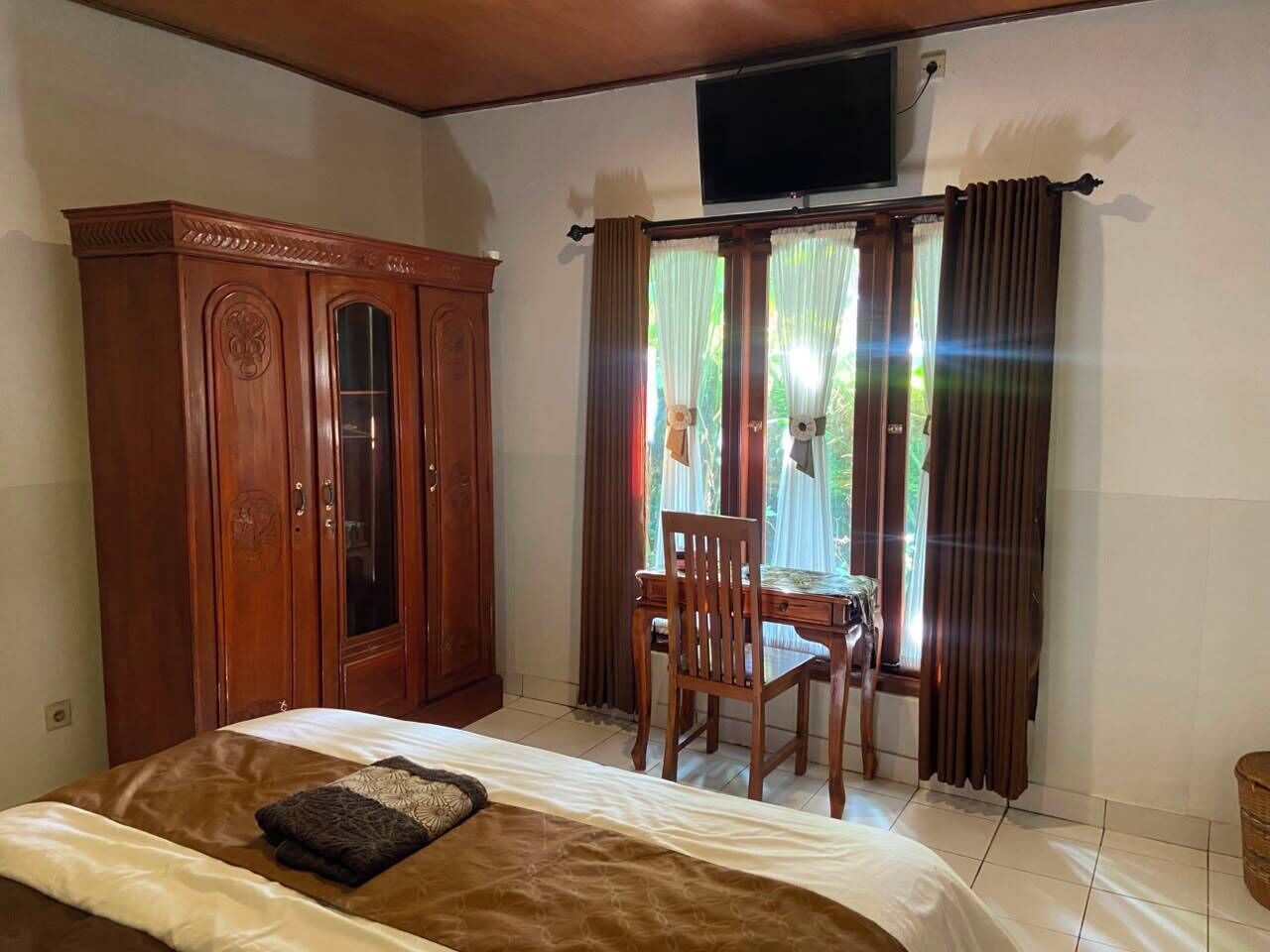 Een slaapkamer met een bed, een houten kledingkast, een bureau met stoel, en een raam met gordijnen.