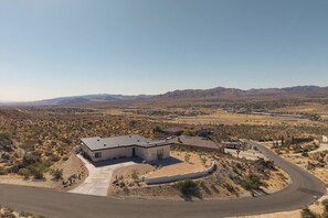 Une maison moderne avec un toit plat, entourée d’un paysage désertique et bordée de montagnes à l’horizon.