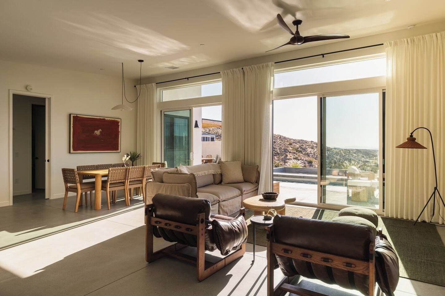Un salón amplio con un gran ventanal, ventilador de techo y un comedor con mesa y sillas.