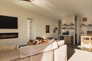 A modern living room with a fireplace, a sofa, and a dining area with wooden furniture. - Pool, Spa, Sauna, Sunken Fire Pit, Amazing Views (Yucca Valley)
