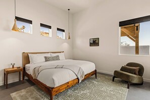 A bedroom with a wooden bed, bedside tables, a chair, and a large window with a view. - Pool, Spa, Sauna, Sunken Fire Pit, Amazing Views (Yucca Valley)