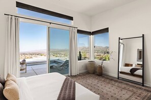 Quarto de hotel com uma cama grande, área de estar com vista e varanda com piscina.