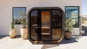 A modern building with a glass door entrance, potted plants, and a view of the surrounding landscape. - The Mandarin - Pool, Spa, Sauna, Sunken Fire Pit, Amazing Views (Yucca Valley)