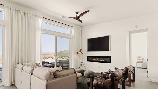 A modern living room with a sofa, a coffee table, a fireplace, and a television mounted on the wall. - The Mandarin - Pool, Spa, Sauna, Sunken Fire Pit, Amazing Views (Yucca Valley)