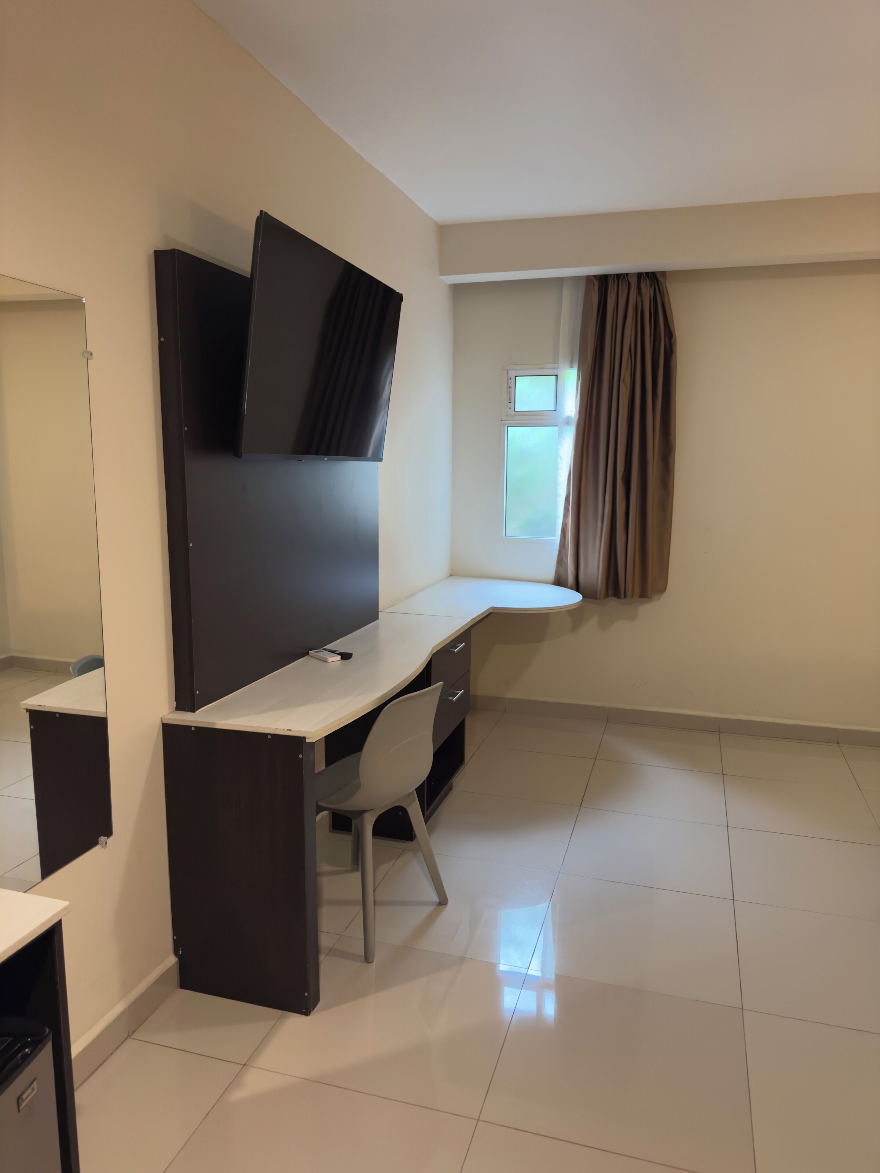 A room with a desk, chair, television, and a window with curtains.