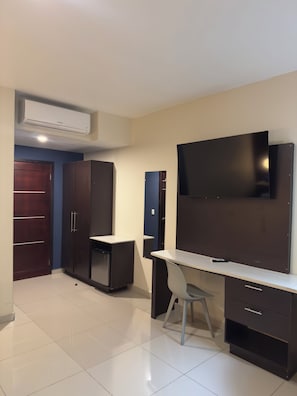A room with a desk, chair, wardrobe, and a mounted television. - Merendón Suites (San Pedro Sula)