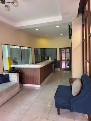 A modern living room with a sofa, a coffee table, and a kitchen area with a counter and appliances. - Merendón Suites (San Pedro Sula)