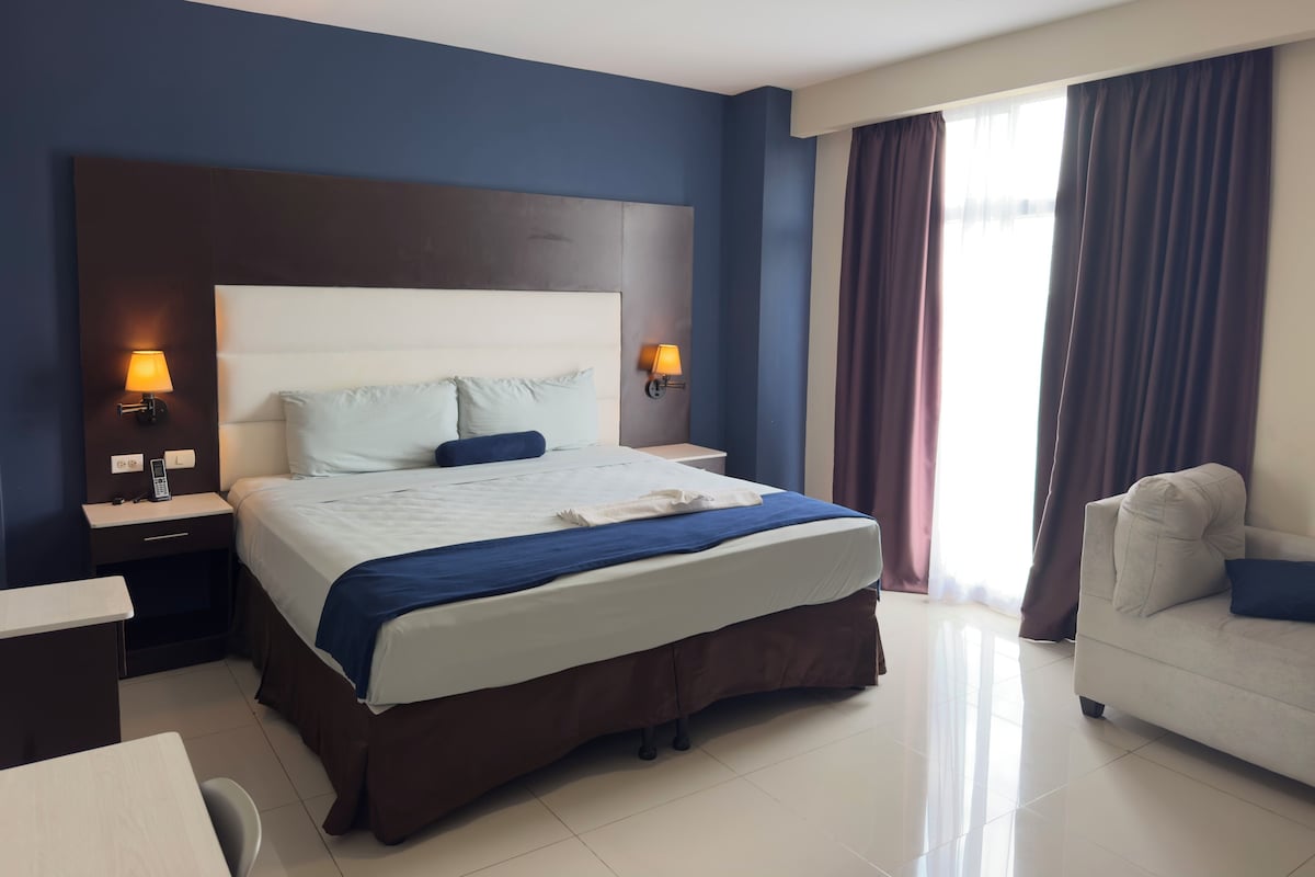 A hotel room with a large bed, bedside lamps, a desk, and a chair.