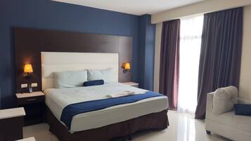 A hotel room with a large bed, bedside lamps, a desk, and a chair.