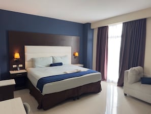 A hotel room with a large bed, bedside lamps, a desk, and a chair. - Merendón Suites (San Pedro Sula)