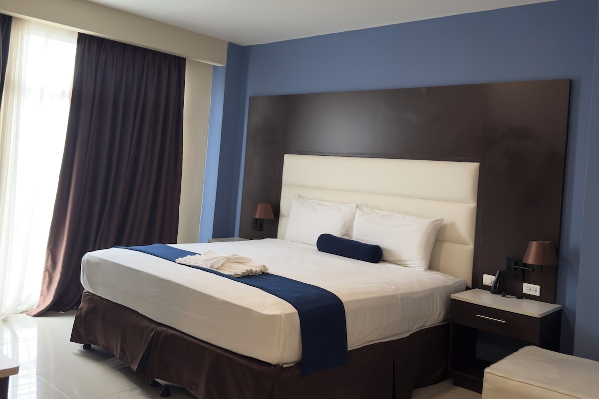 A hotel room with a large bed, bedside tables, a desk, and a chair.