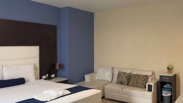 Quarto de hotel com cama, sofá, mesa de cabeceira, luminária e lixeira.