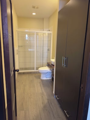 A bathroom with a glass-enclosed shower, a toilet, and a cabinet. - Merendón Suites (San Pedro Sula)