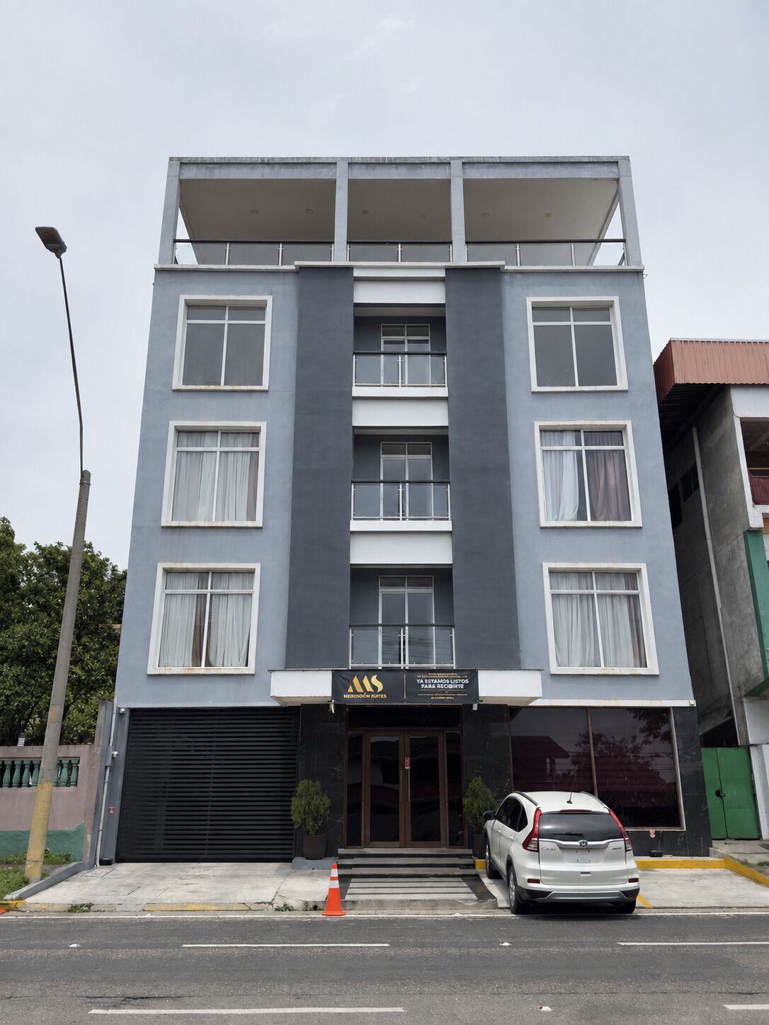 A multi-story hotel with a modern facade, a black garage door, and a white car parked in front.
