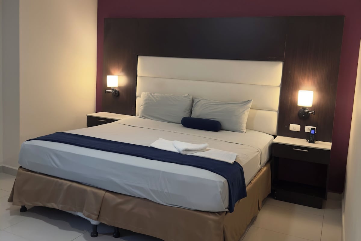 A neatly made bed with a headboard, two bedside tables with lamps, and a tiled floor.