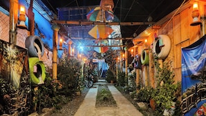 Un étroit sentier bordé de murs décorés de pneus et illuminé de lanternes suspendues, qui mène à une zone abritée d’où l’on peut admirer un plan d’eau.