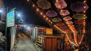 Un hôtel appelé «Hôtel Xuana», avec une enseigne, un escalier menant à l’entrée et une rue bordée de parasols et d’éclairages.