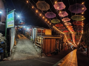 A hotel named 'Hotel Xuana' with a signboard, a staircase leading to the entrance, and a street lined with umbrellas and lights.