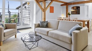 A modern living room with a sofa, chairs, a glass coffee table, and a dining area with a table and chairs.