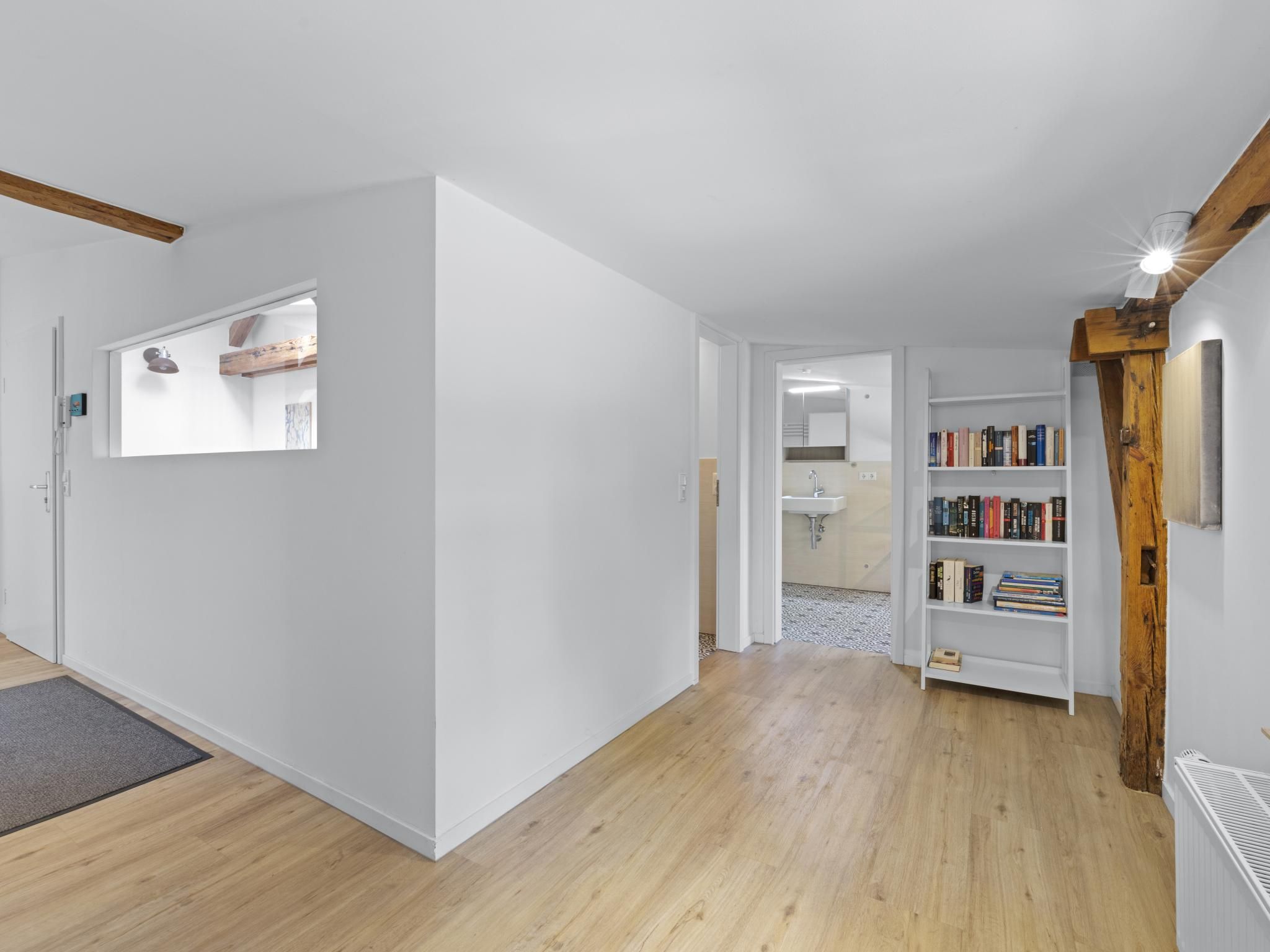 Een gang met een houten vloer, witte muren, een boekenkast en een deur naar een badkamer.