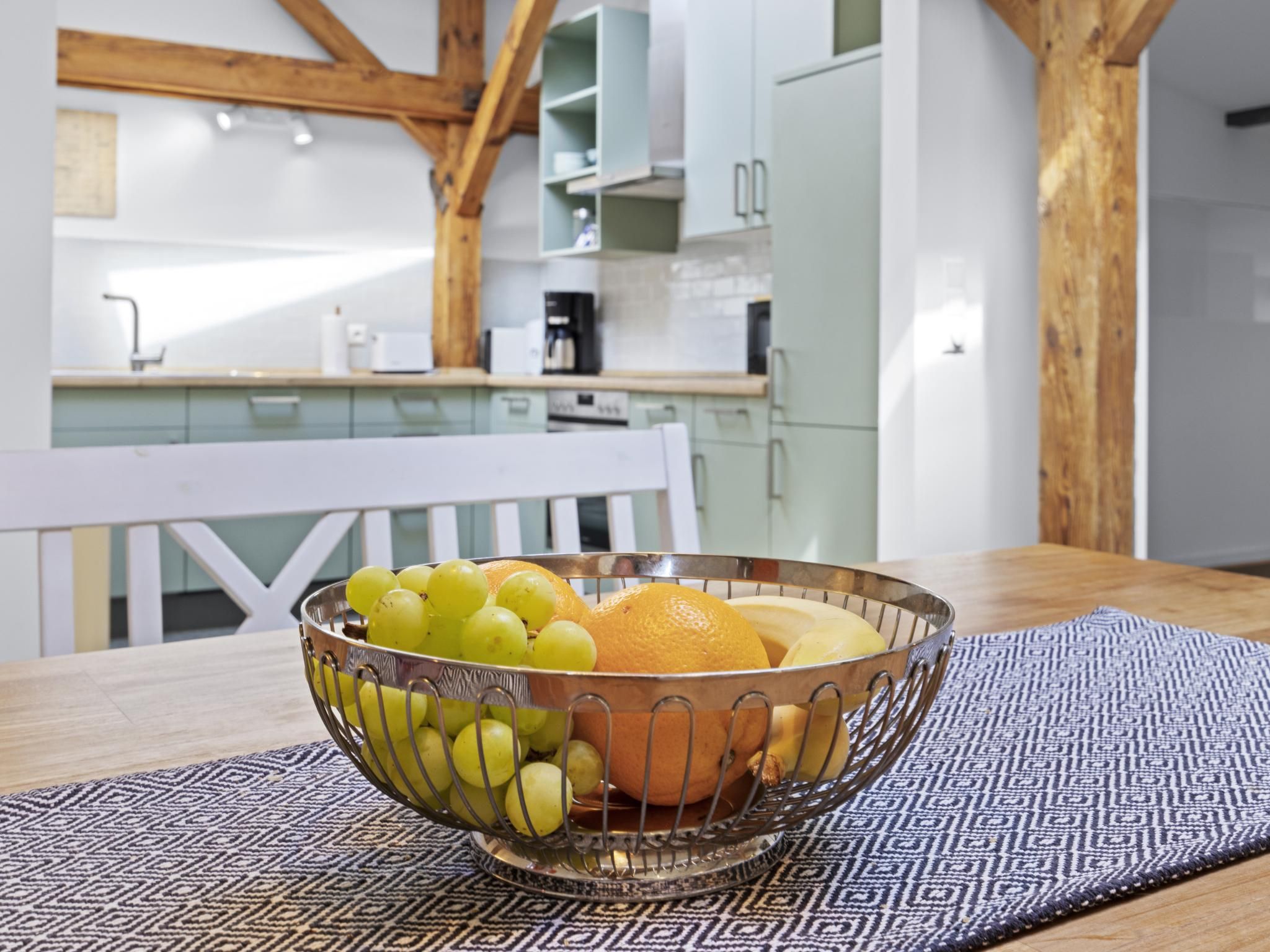 A kitchen with white cabinets, a wooden ceiling, and a fruit bowl on a table.
