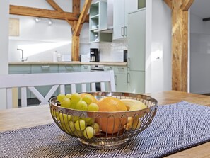 A kitchen with white cabinets, a wooden ceiling, and a fruit bowl on a table.