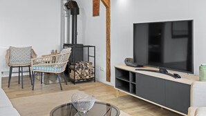 A modern living room with a TV, wooden beams, a fireplace, and a dining area with wicker chairs.
