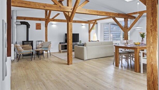A spacious living area with exposed wooden beams, a sofa, a dining table with chairs, and a television.