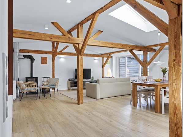 A spacious living area with exposed wooden beams, a sofa, a dining table with chairs, and a television.