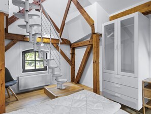 A room with a white cabinet, a window with a view, a white bed, and a wooden ceiling structure.