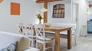 A dining area with a wooden table and white chairs, a hanging light fixture, and a window with a view.