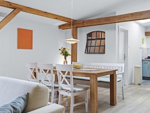 A dining area with a wooden table and white chairs, a hanging light fixture, and a window with a view.