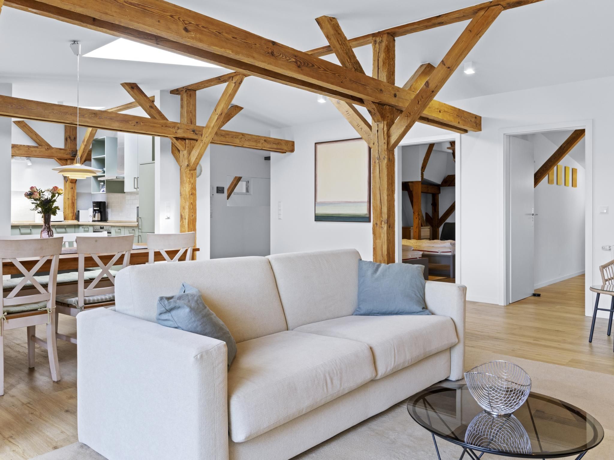 Een moderne woonkamer met een witte bank, een glazen salontafel en zichtbare houten balken.