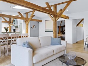 A modern living room with a white sofa, a glass coffee table, and exposed wooden beams.