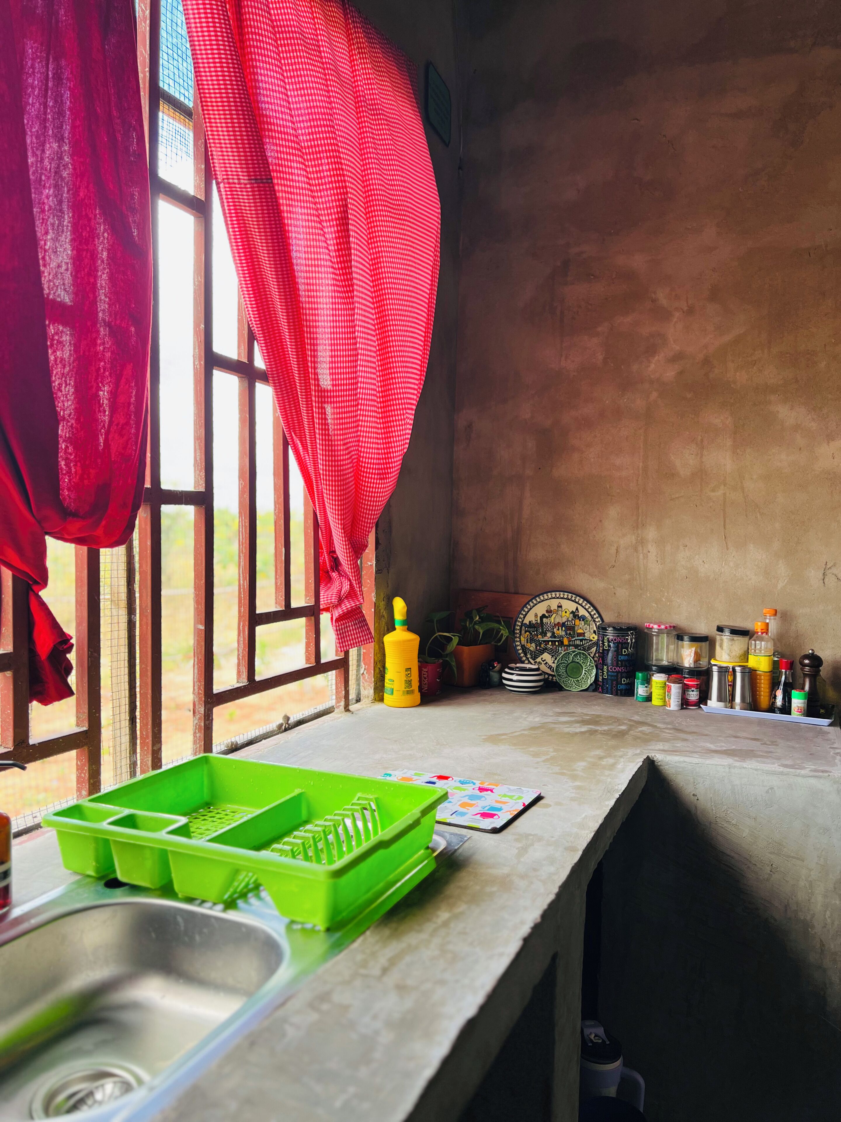 Una cocina con un lavabo, un escurreplatos verde y varios utensilios de cocina sobre la encimera.
