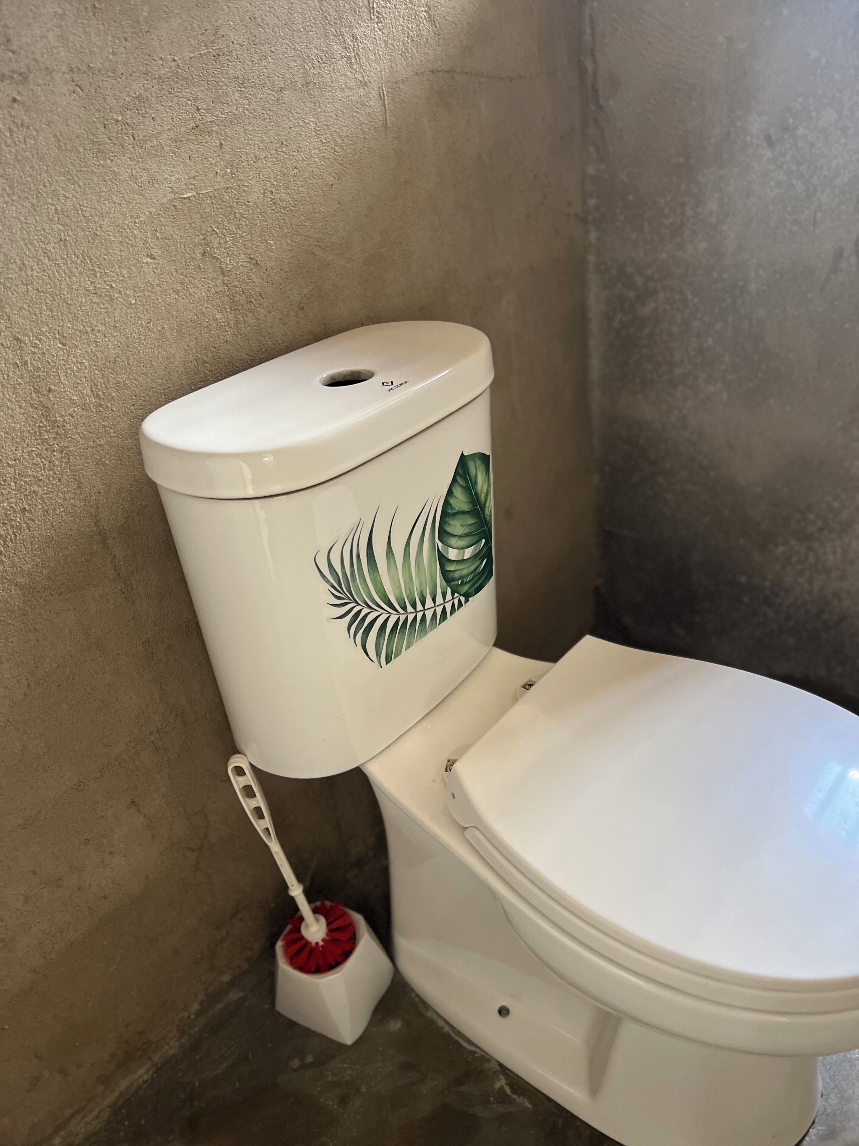 Lavabo amb una calcomania de fulla i una escobella de lavabo vermella.