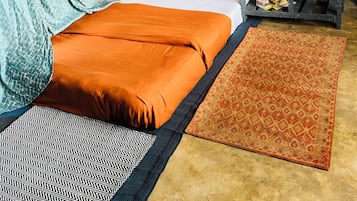 Ein Zimmer mit einem Bett, einem kleinen Tisch mit weißem Tuch, einem gemusterten Teppich und einer wandmontierten Vorrichtung.